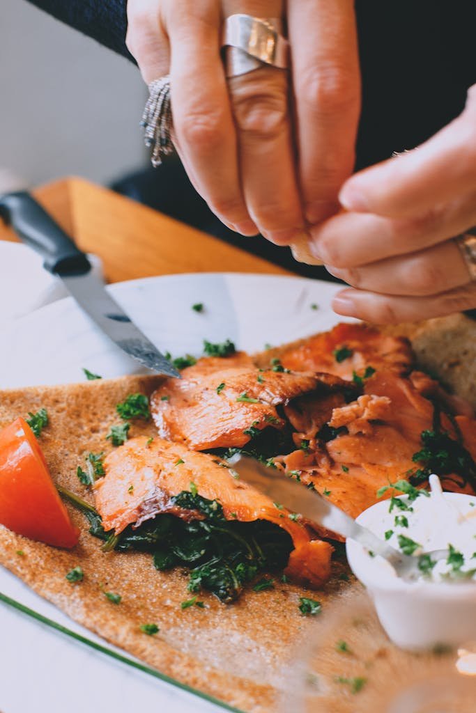 Close-up of a hand preparing a delicious salmon crepe with garnishes.