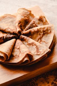 Close-up of freshly made crepes displayed on a wooden board, captured in warm and inviting tones.